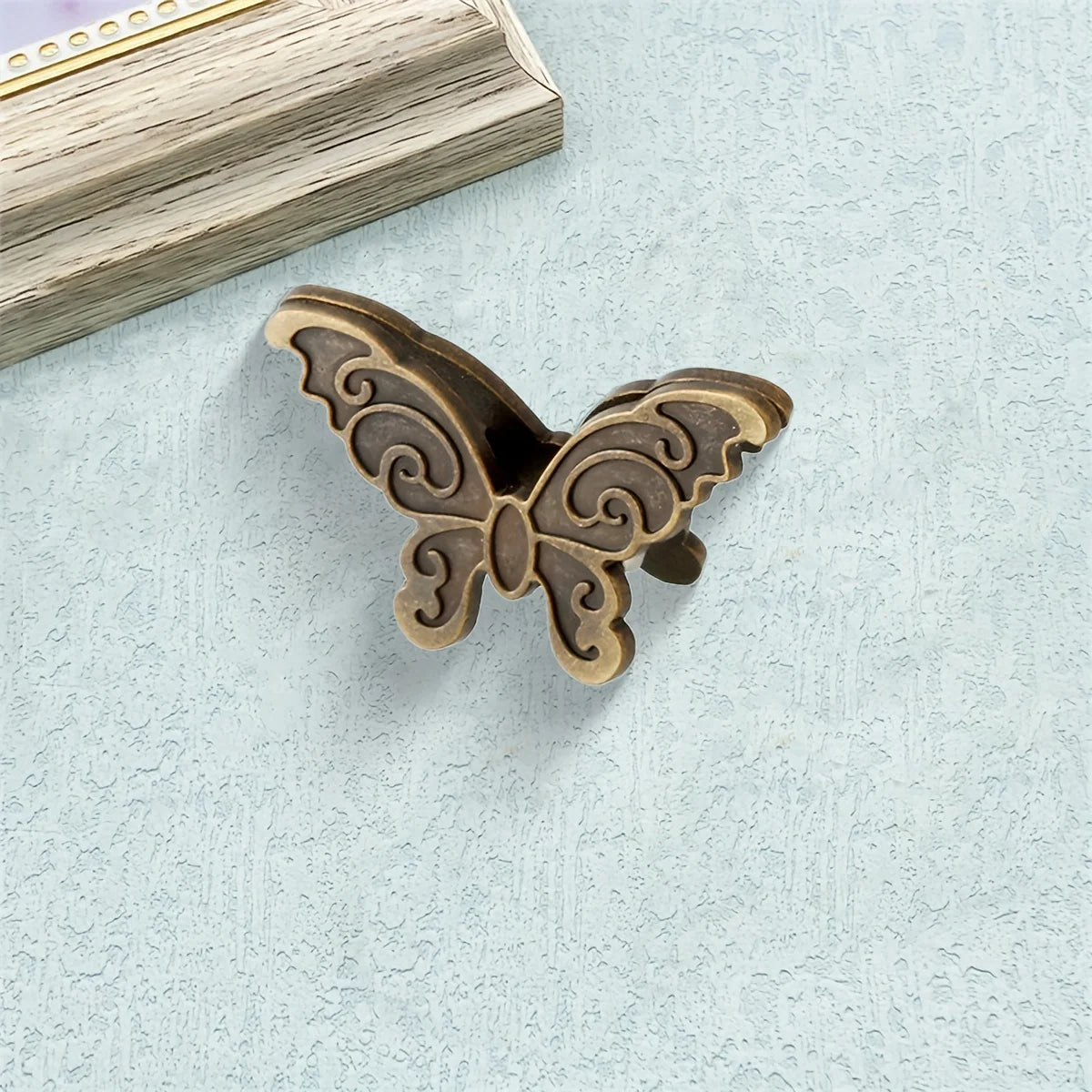 A vintage bronze butterfly metal book clip resting on a light blue textured surface.