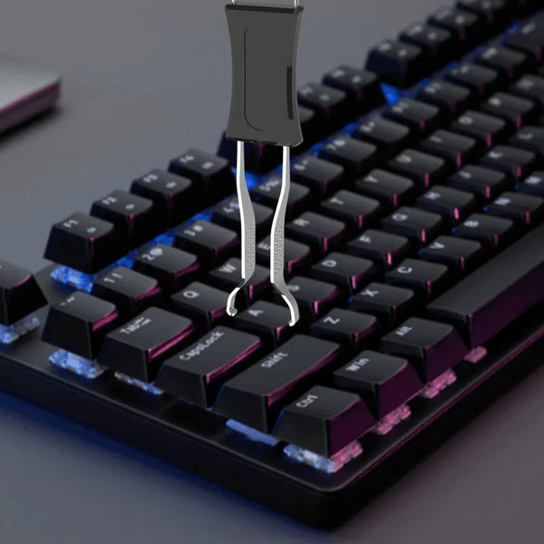 Gros plan d'un clavier mécanique noir avec un outil d'extraction de capuchon métallique inséré dans une touche.