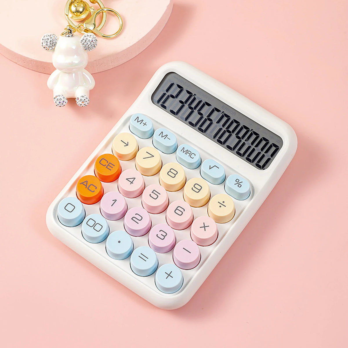 A white mechanical 12-digit calculator with round keys is shown on a pink background next to a small white bear figurine.