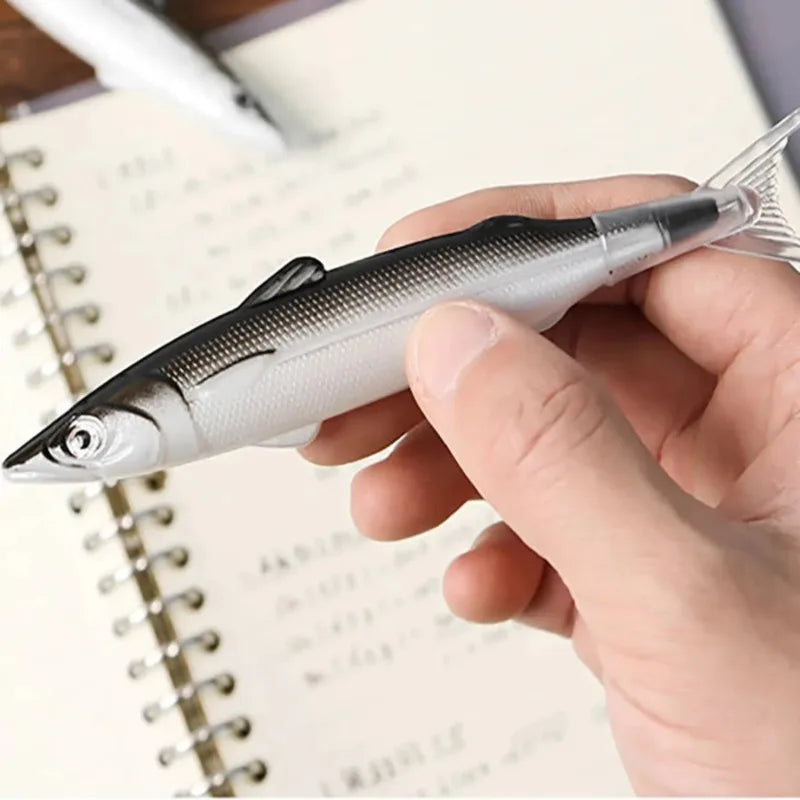 A hand holds a silver and black ocean fish ballpoint pen resting on lined paper.