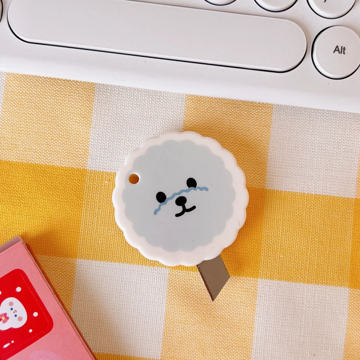 A white cat paw-shaped mini cutter is shown on a yellow and white checkered surface next to a computer keyboard.