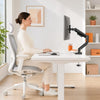 A woman sits at a white desk using a premium single monitor desk mount with gas spring arm for computer work.