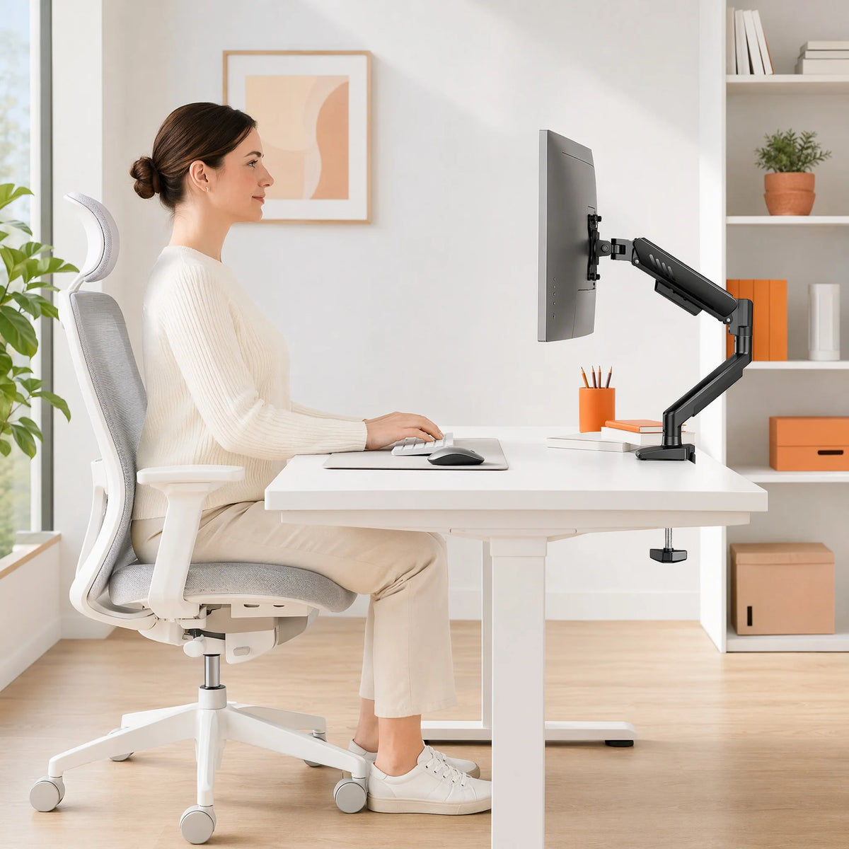 A woman sits at a white desk using a premium single monitor desk mount with gas spring arm for computer work.