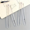 A set of precision acrylic folding rulers and a black pen are displayed on a lined paper with geometric drawings.
