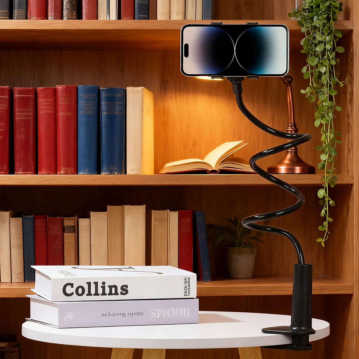 A black adjustable tablet and phone holder with a copper base is displayed next to a bookshelf.