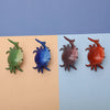 Quatre porte-stylos crabes colorés et fantaisistes en vert, bleu, marron et orange sur fond clair.