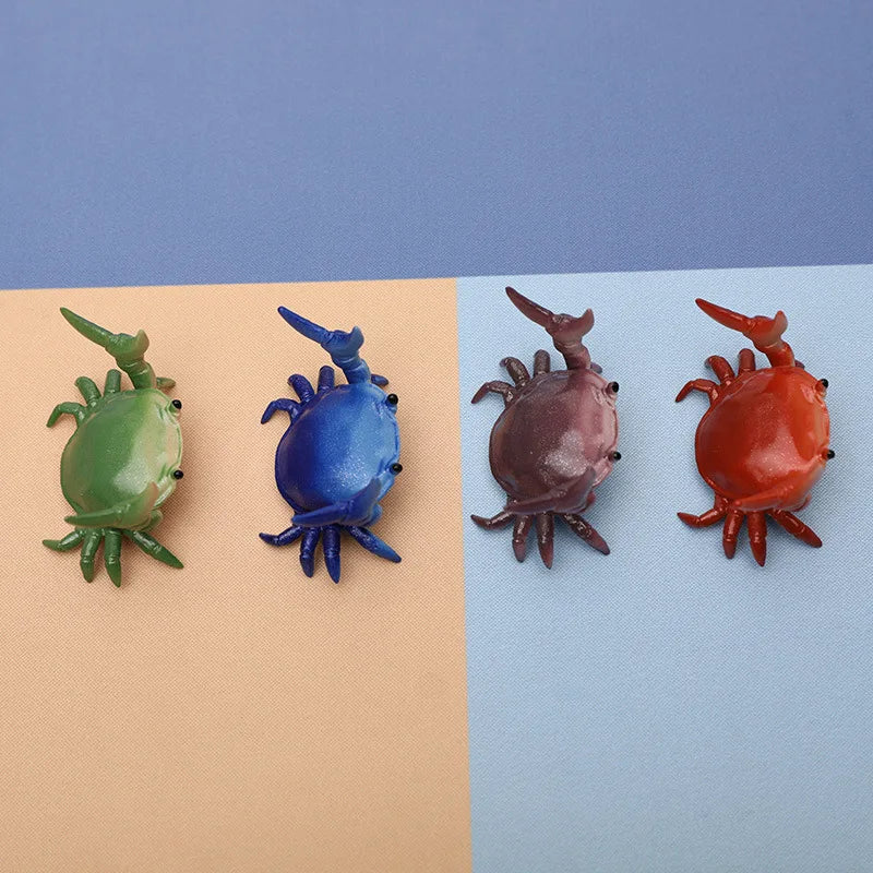 Quatre porte-stylos crabes colorés et fantaisistes en vert, bleu, marron et orange sur fond clair.
