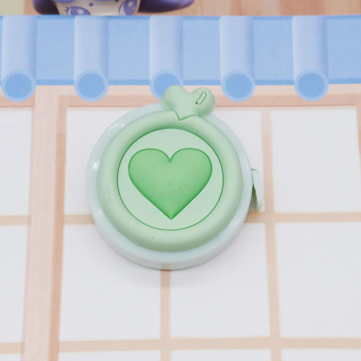 Una cinta métrica corazón retráctil y compacta de cuerpo verde claro sobre un fondo de cuadrícula.