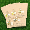 Five small yellow and black ladybug and daisy keychains are displayed on light brown cards.