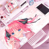 A close-up of an anime-style illustration of a pink-haired girl on a desk mat with various stationery items.