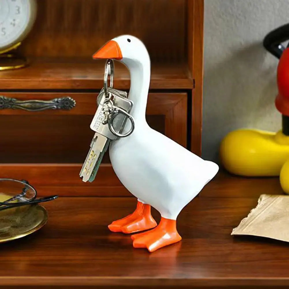 A white ceramic duck figurine with orange feet is shown holding a set of keys on a wooden desk.
