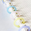 A series of colorful reusable plastic binding rings in shades of white, purple, blue, and yellow arranged diagonally on a whi