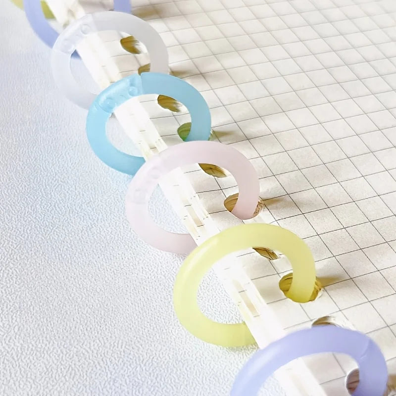 A series of colorful reusable plastic binding rings in shades of white, purple, blue, and yellow arranged diagonally on a whi