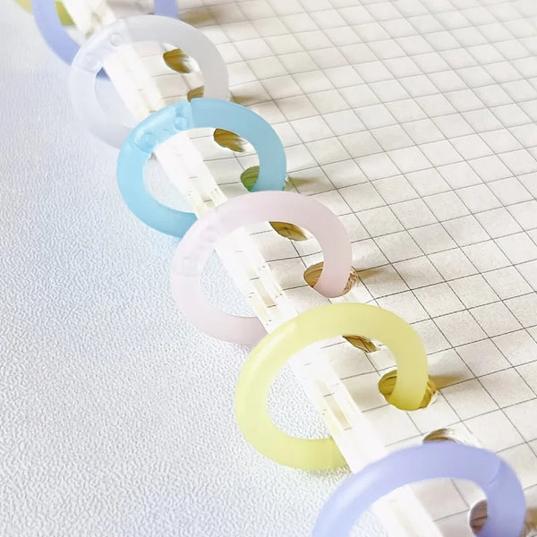 A series of colorful reusable plastic binding rings in shades of white, purple, blue, and yellow arranged diagonally on a whi