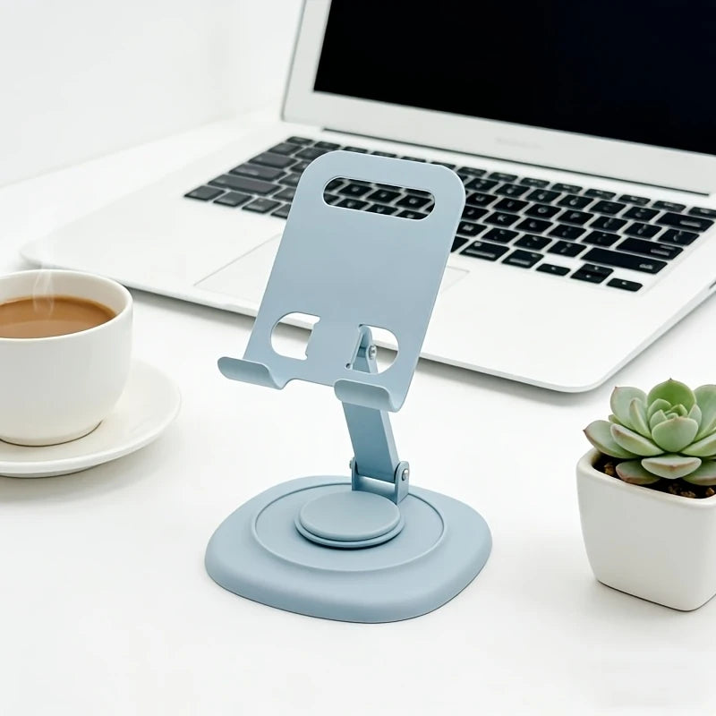 A light blue foldable desktop phone stand is shown next to a laptop and a cup of coffee.