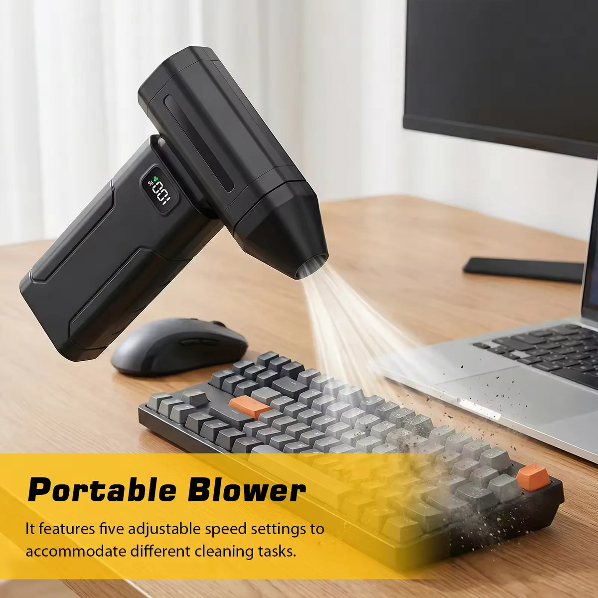 Un soplador portátil negro junto a una laptop y un cepillo de limpieza texturizado sobre un escritorio de madera.