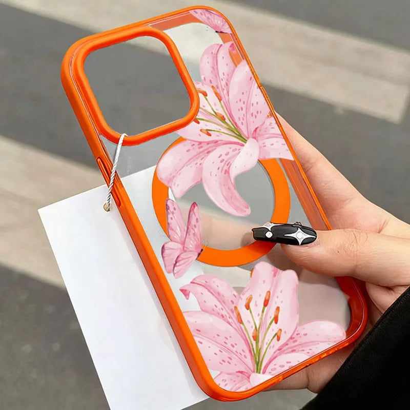 A hand holds a transparent orange iPhone case featuring a pink lily floral design.