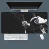 A black gaming mousepad with an illustration of a hand wielding a sword against a starry background, shown with a monitor and