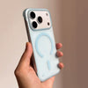 A hand holds a light blue slim magnetic phone case for an iPhone, featuring a circular cutout design.