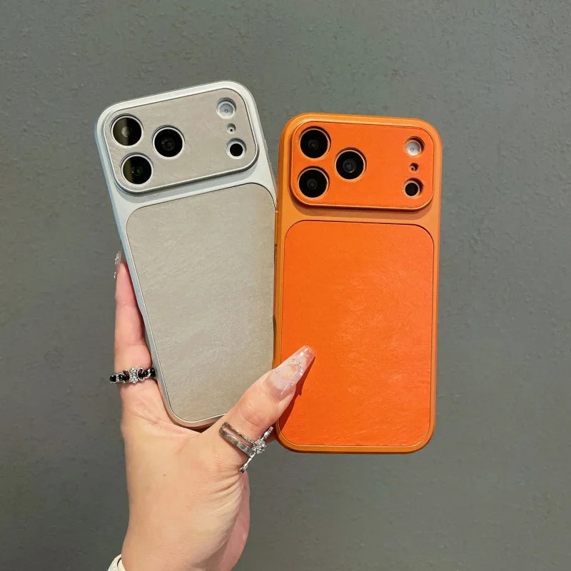 A hand holds two phone cases, one silver and one orange, against a gray background.