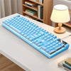 A blue low profile wired gaming keyboard with a numeric keypad is displayed on a white desk.