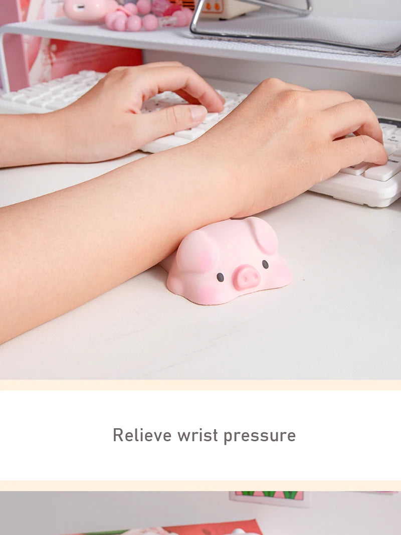 Pink piggy shaped ergonomic wrist rest placed on a white desk next to hands typing on a computer.