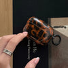 A hand holds a glossy tortoiseshell protective case for AirPods against a dark background.