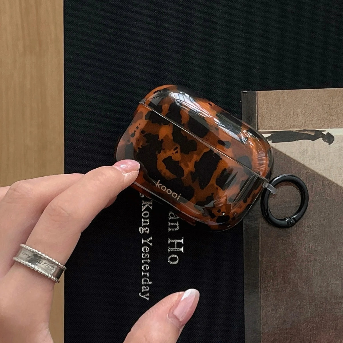 A hand holds a glossy tortoiseshell protective case for AirPods against a dark background.