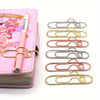 A collection of mixed color heart-shaped metal pen clips arranged in a vertical row.