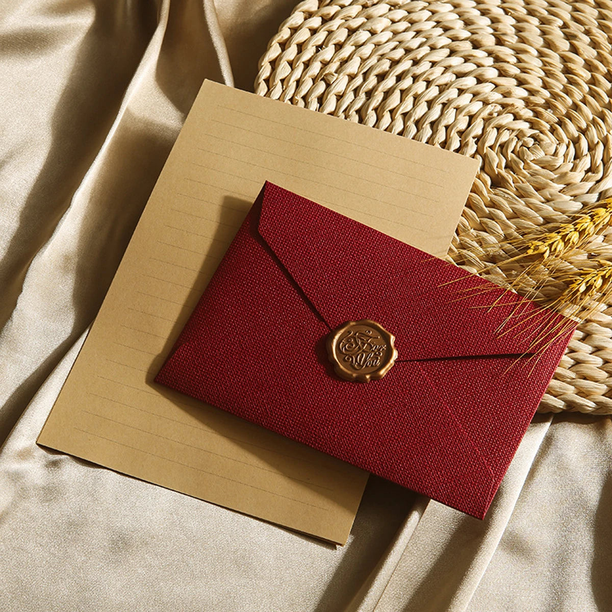 Ein Set aus zwei kraftpapierumschlägen, einer rot und einer beige, mit Wachssiegel, auf einer geflochtenen Matte.