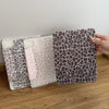 A hand holds a stack of leopard print leather cases for an iPad, featuring various shades and patterns.