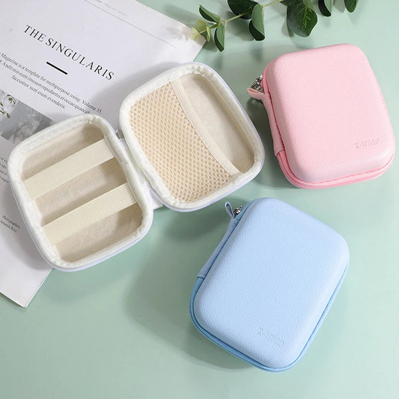 A pink leather storage pouch organizer with a clear insert and a light blue leather pouch are displayed on a green surface.