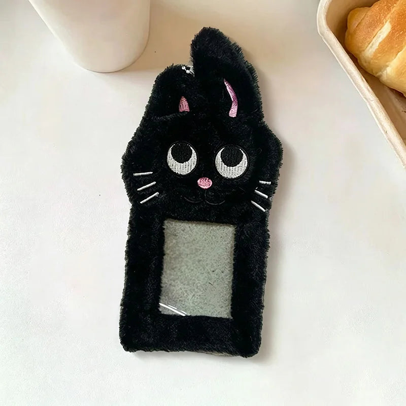 A black plush cat photocard holder with pink accents and a clear window is displayed on a white surface.