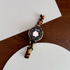 A close-up photo of a resin beaded watch with a brown and black pattern on the band and a round face displaying 14:23.