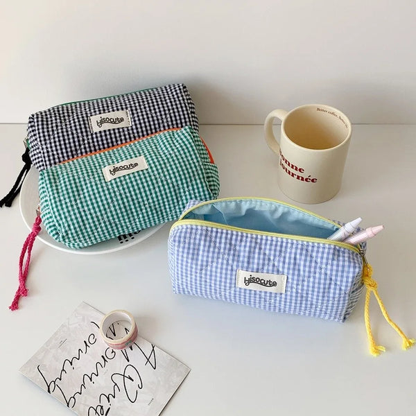Una colección de tres estuches de lápices de tela con patrones a cuadros verdes, azules y morados, junto a una taza blanca