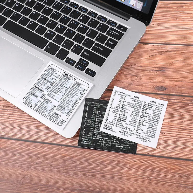 A laptop keyboard with a Windows shortcut quick reference sticker placed on a wooden table.
