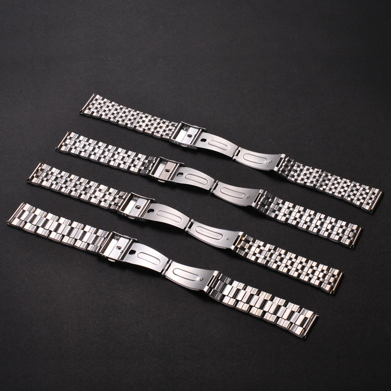 A collection of stainless steel watch bands with folding safety clasps laid diagonally on a dark surface.