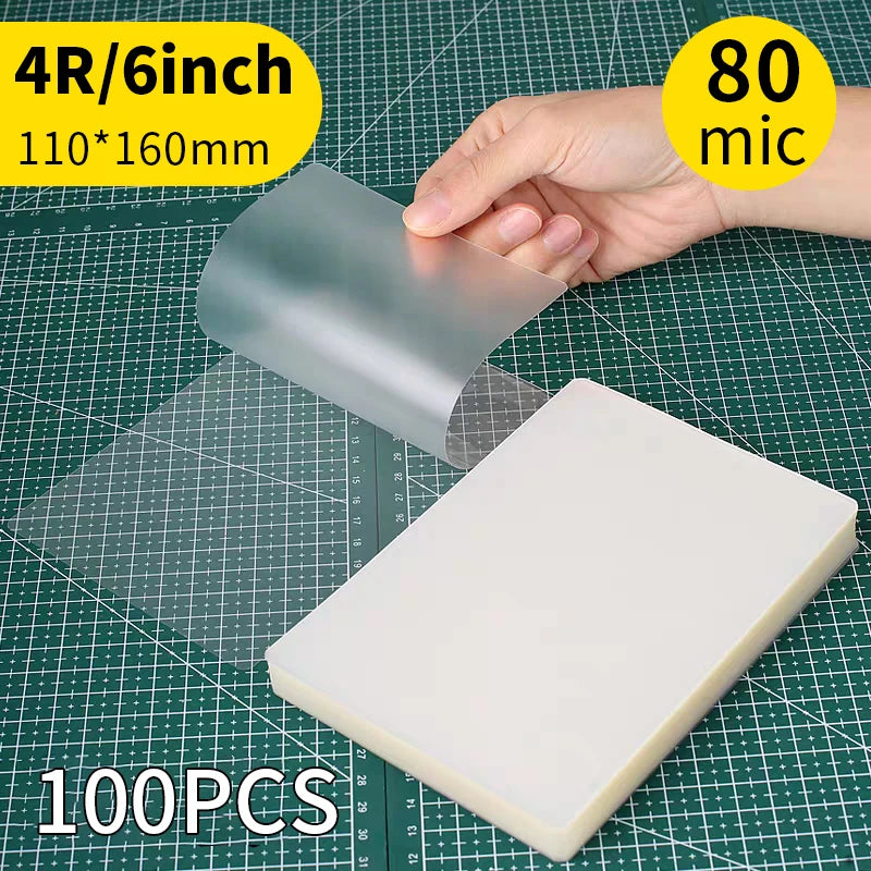 A hand holds a clear thermal laminating pouch, showing its size and material against a grid background.