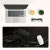 A black desk mat featuring a white line drawing of a large ocean wave and landscape.
