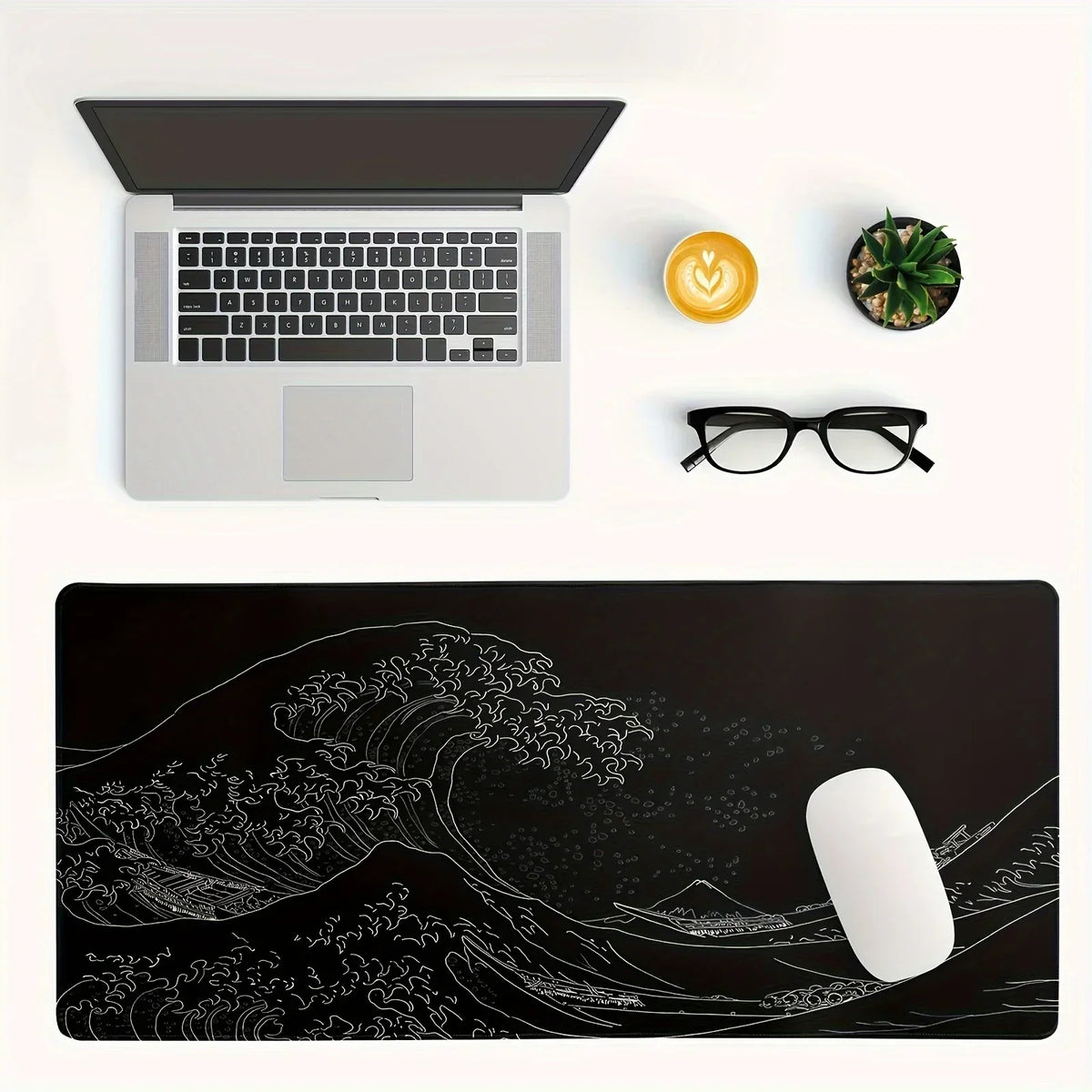 A black desk mat featuring a white line drawing of a large ocean wave and landscape.
