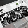 A large gaming mouse pad featuring a black and white liquid wave design placed on a desk.