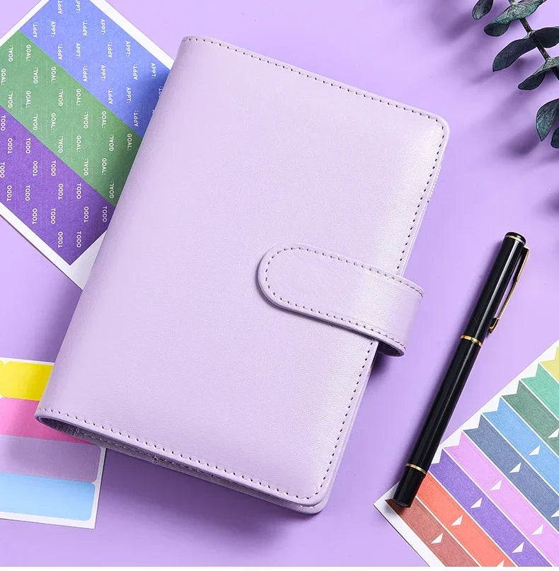 A purple A6 budget planner with a leather cover and envelope system resting on a purple surface.
