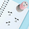 A pink self-inking rubber stamp with a funny meme face design is placed on a white notepad.