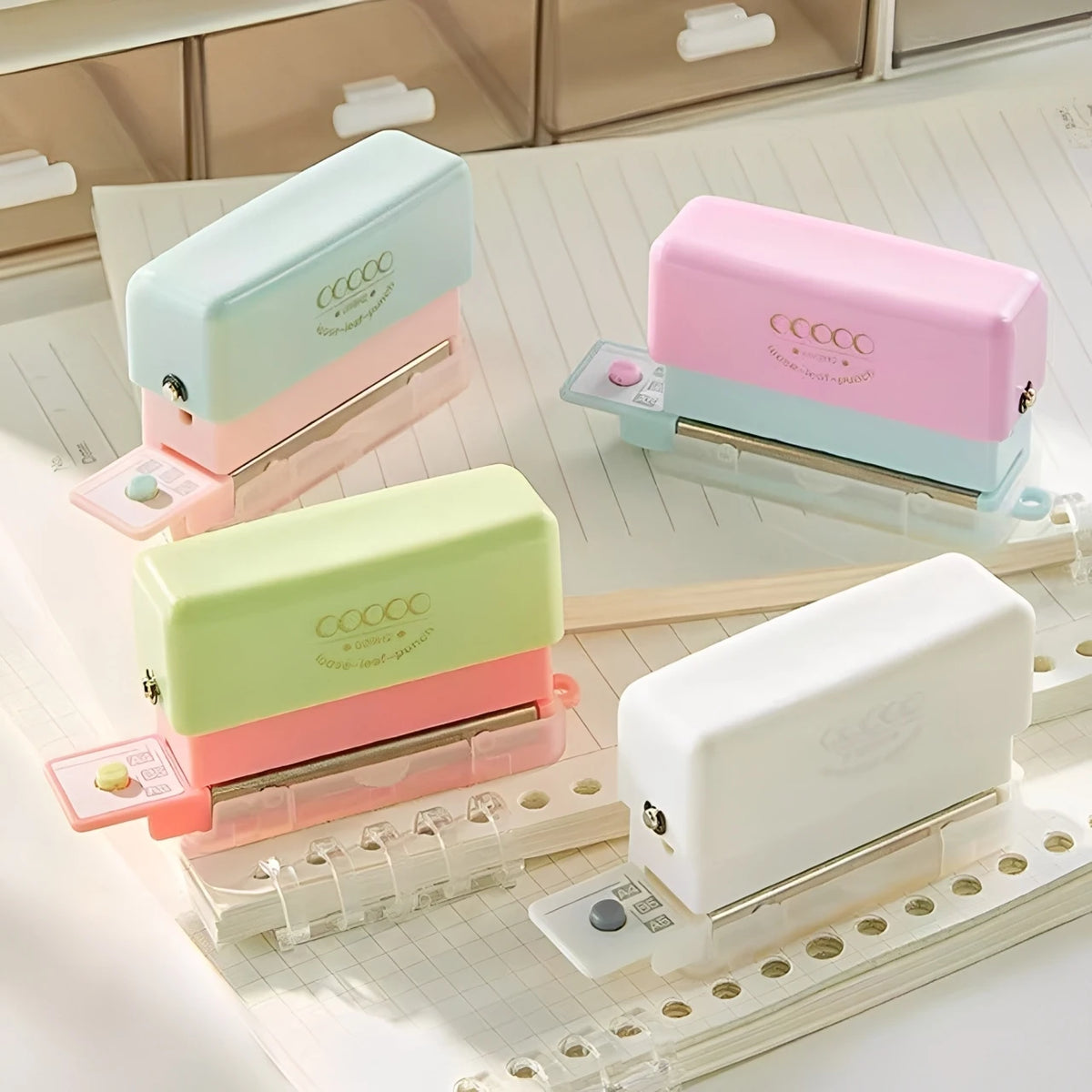 A set of mini multi-hole punches in pastel pink and mint green are displayed on a white sheet of paper.