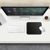 A black portable gaming mouse pad with a stitched edge is placed on a white desk next to a computer monitor and keyboard.