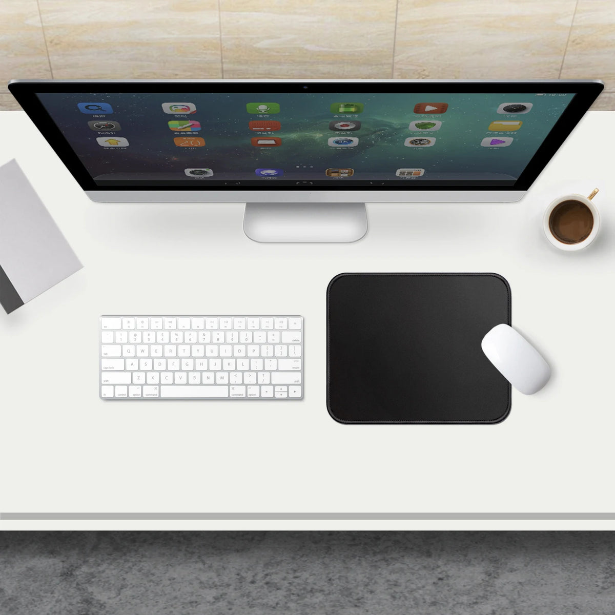 A black portable gaming mouse pad with a stitched edge is placed on a white desk next to a computer monitor and keyboard.