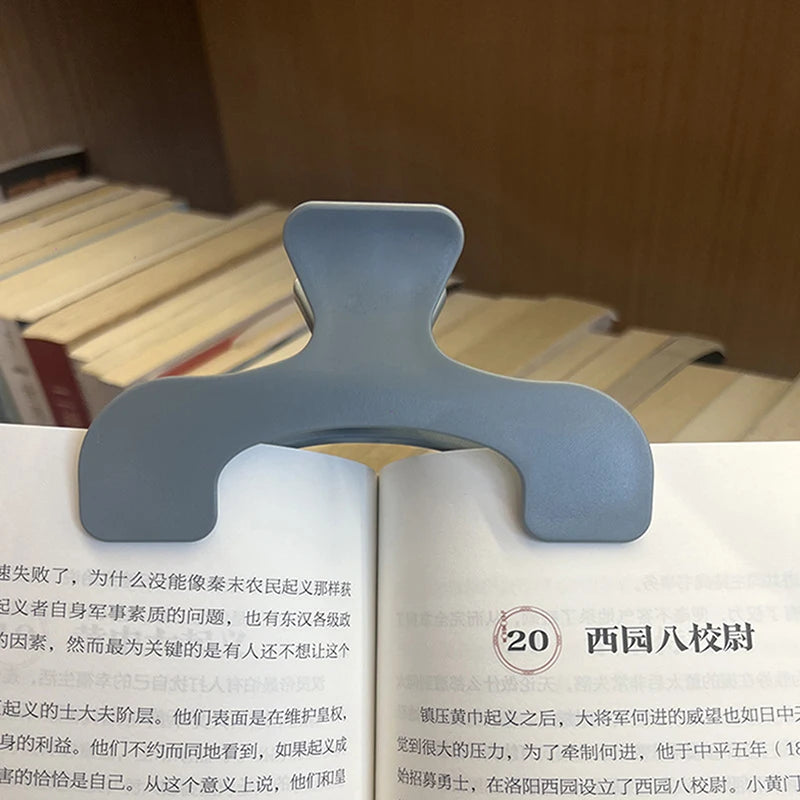 A close-up of a light gray book page clip used to hold open a transparent book page.