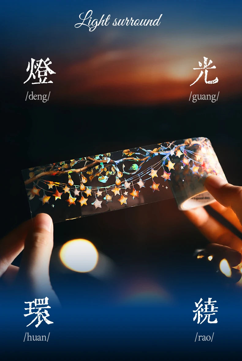 A hand holds a roll of decorative PET washi tape featuring gold and iridescent floral designs against a dark background.