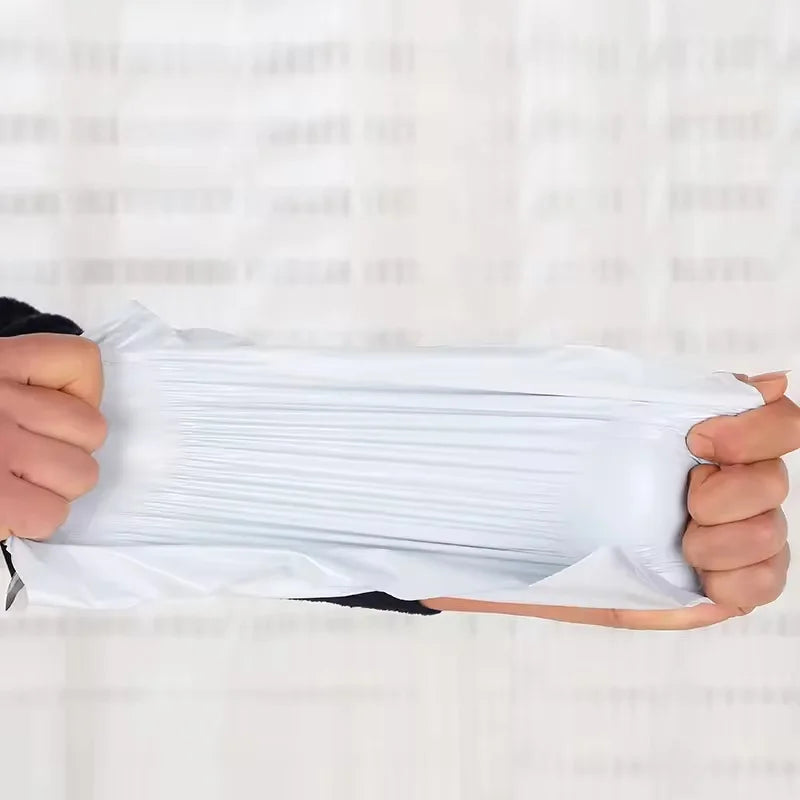 A hand is holding a stack of clear plastic mailing bags for shipping.