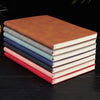 A stack of five premium A5 leather journals or diaries in various shades of brown, blue, pink, and red.